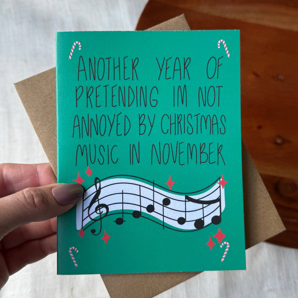 A hand holds a teal Christmas greeting card with the text &