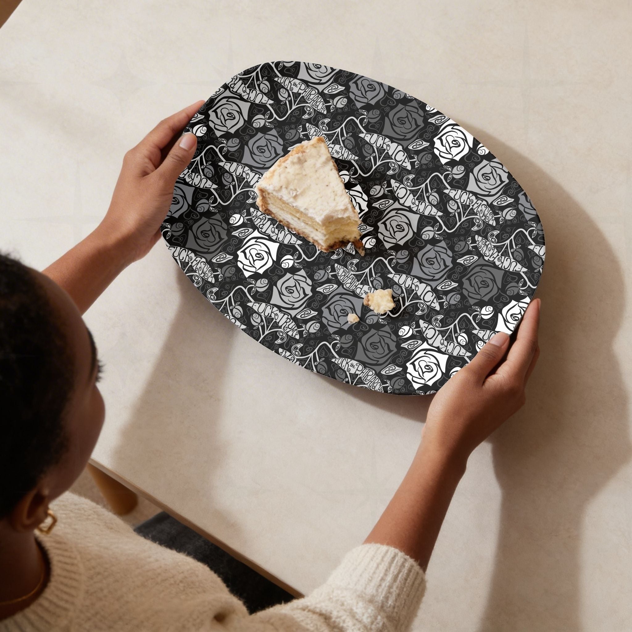 Overhead view of feminist hidden profanity serving platter with slice of cake showing dark gothic rose pattern with protest banners held from above on cream surface