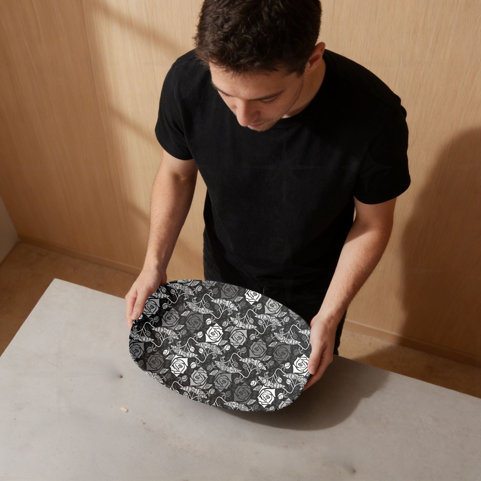 Person in black shirt holding feminist hidden profanity serving platter showing black and white gothic rose pattern with hand lettered banners on warm wood surface