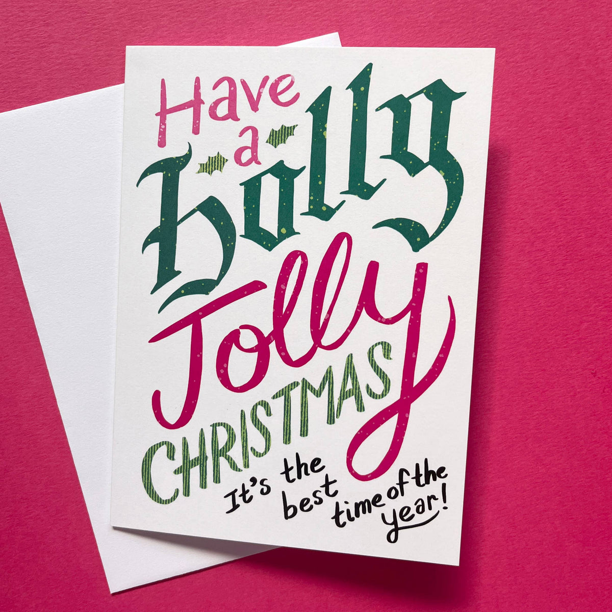 A white Christmas greeting card with festive hand-lettered text reading &