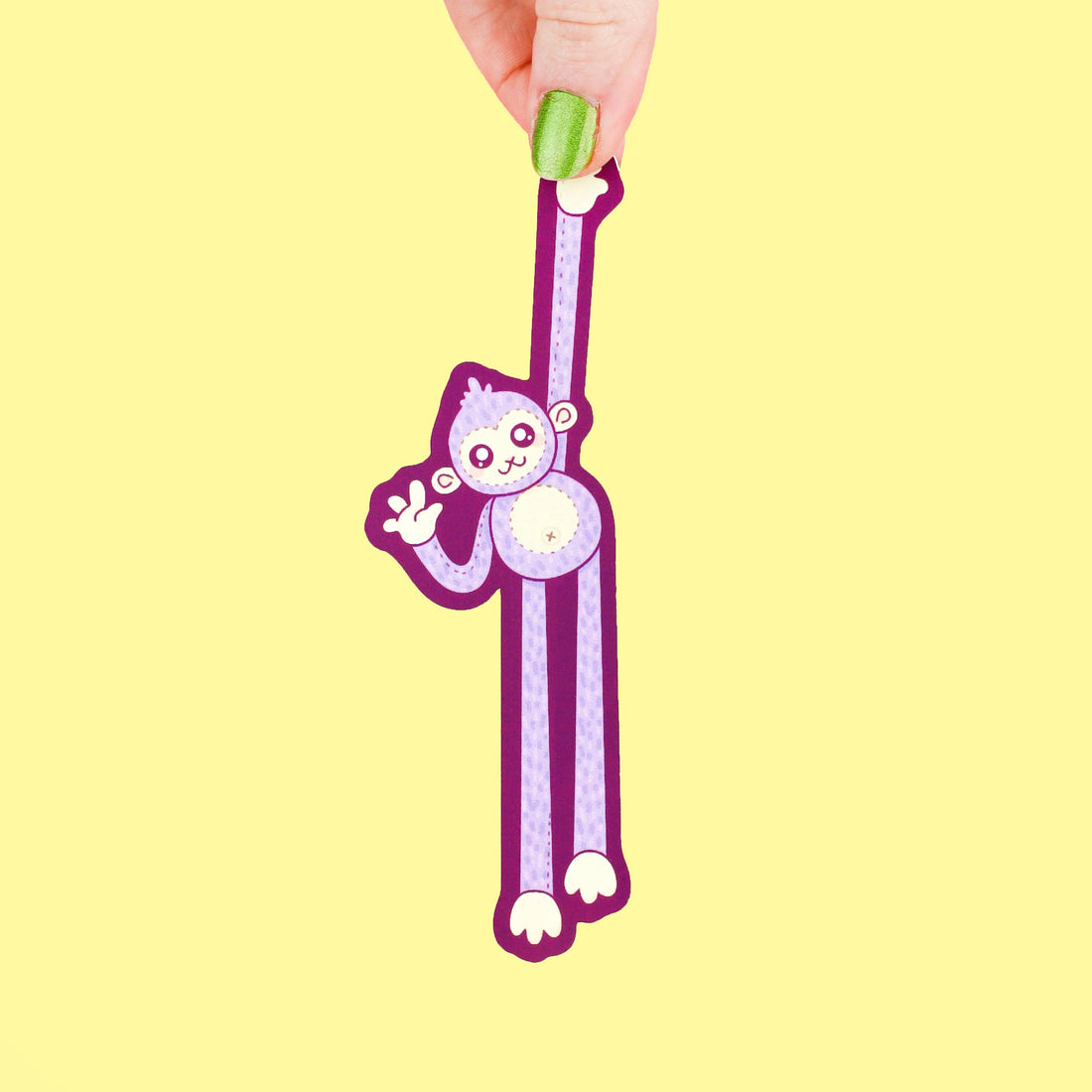 Hand holding a purple monkey-shaped bookmark on a yellow background