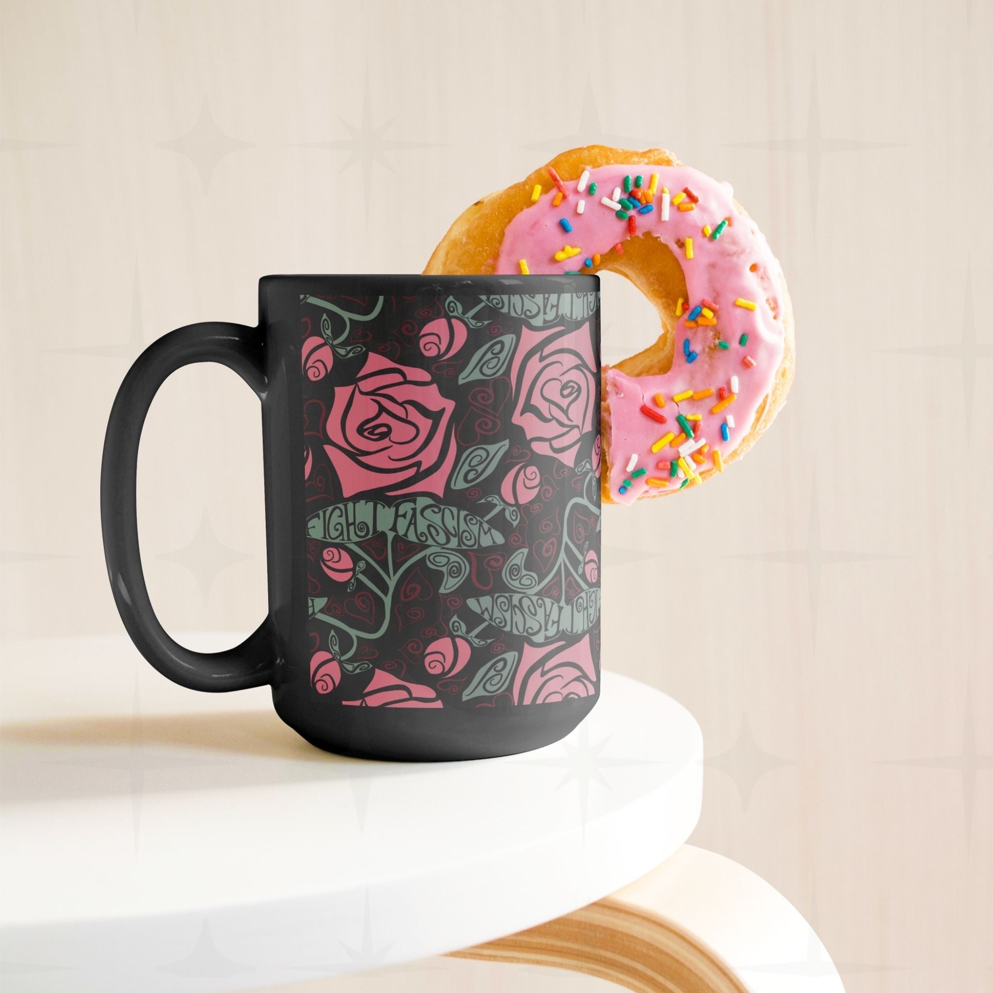 15oz Fight Fascism black ceramic mug styled beside a sprinkle donut on a white surface, Art Nouveau floral wrap pattern visible