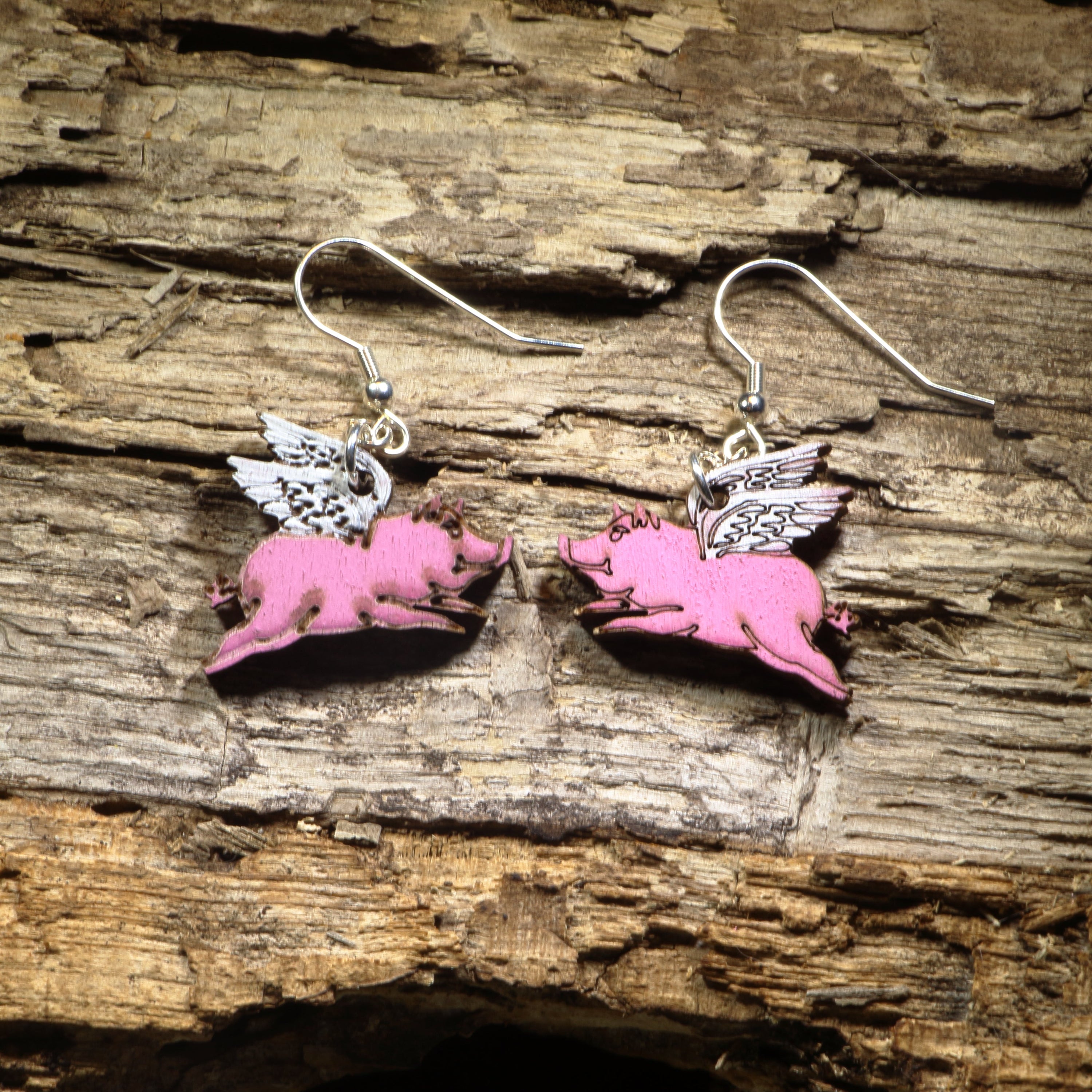 Hand-painted wooden flying pig dangle earrings featuring adorable pink pigs with detailed white wings. Crafted from lightweight wood with hypoallergenic .925 sterling silver hooks, these whimsical earrings are perfect for pig lovers, farm animal fans, fantasy enthusiasts, and anyone who enjoys quirky, humorous jewelry that proves anything is possible when pigs fly.