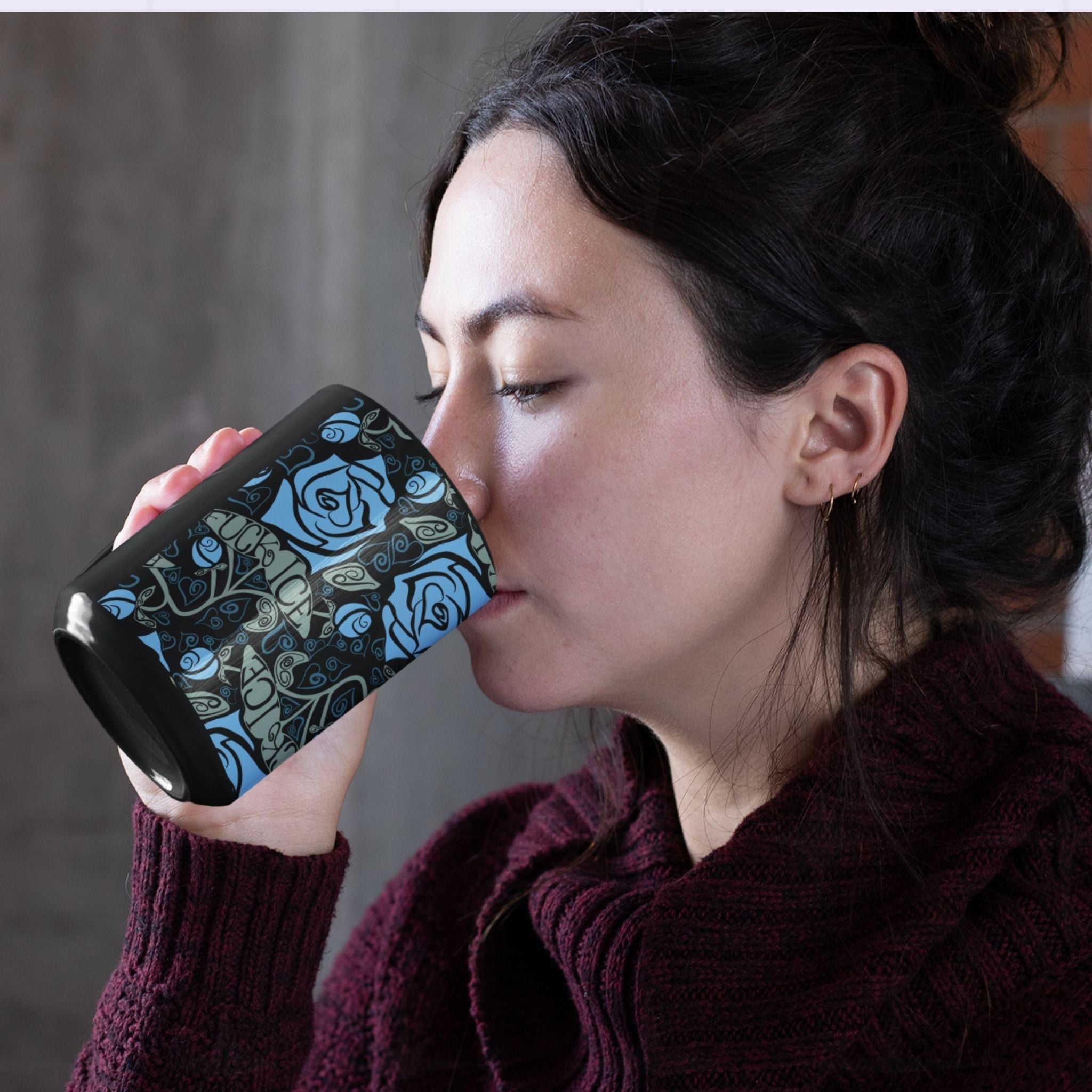 Woman drinking from a dark floral hidden message coffee mug featuring cornflower blue roses and a hidden activist message woven into the botanical pattern on a glossy black ceramic mug