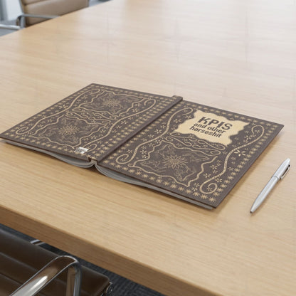 KPI profanity journal lying open flat on conference table beside silver pen showing both covers with vintage equestrian embroidered design
