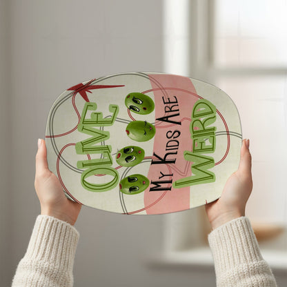 Hands holding up retro mid-century funny serving platter with four cartoon olive faces and Olive My Kids Are Weird hand-lettered typography against bright window background