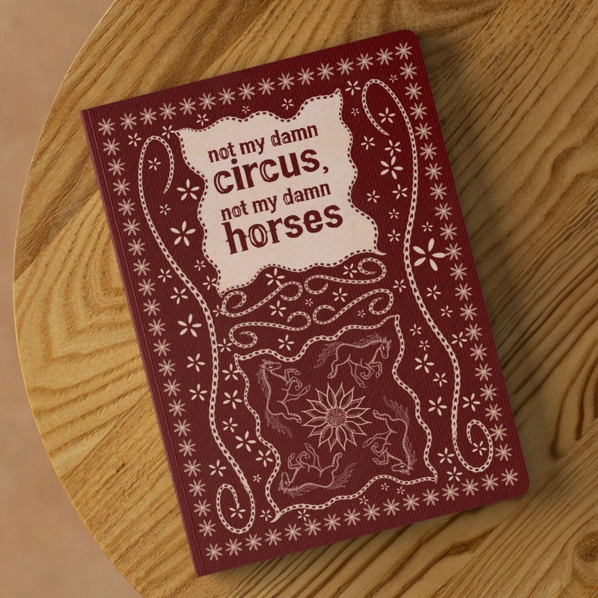 Not my circus folk art lined journal on round wooden table showing burgundy softcover with stitched horse and sunflower illustration