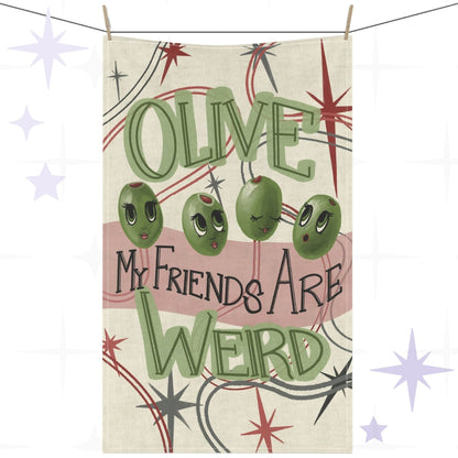 Funny tea towel with retro mid-century olive illustration and hand-lettered pun reading "Olive my friends are weird," hung on a clothesline against a white background