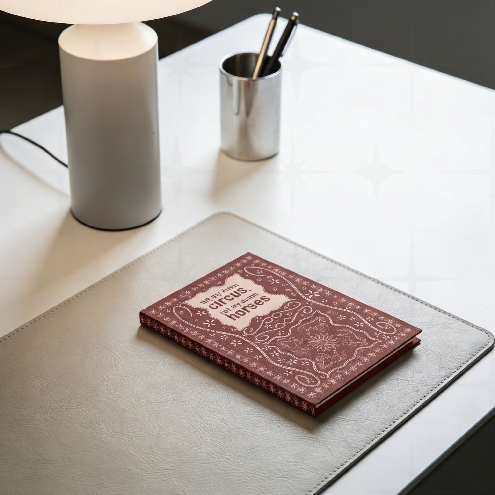 Funny western hardcover journal on leather desk pad beside a modern lamp and pen holder showing stitched leather cover design