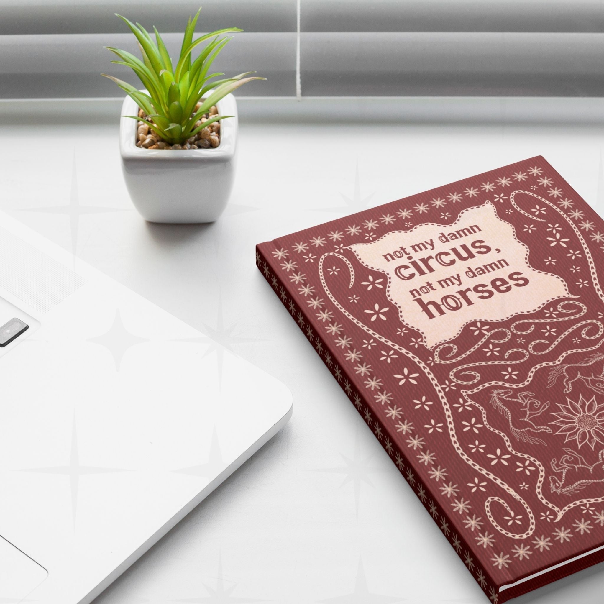 Snarky western journal on white desk next to laptop and small succulent plant showing not my damn circus hand-lettered cover