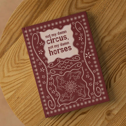 Funny western hardcover journal lying on round wooden surface showing front cover with stitched leather folk art design
