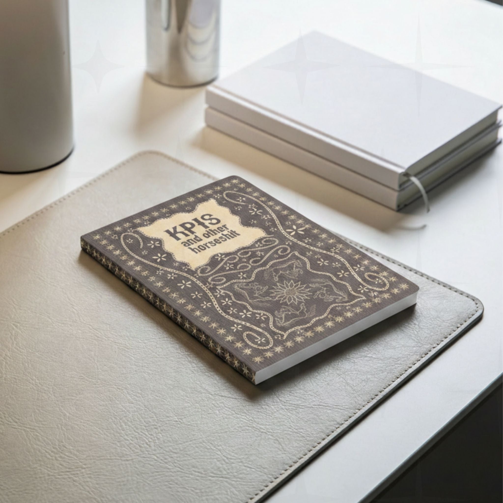 Profanity softcover journal on gray leather desk pad beside notebooks in work from home lifestyle setting