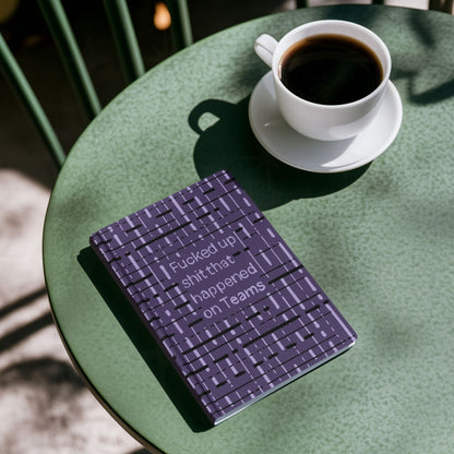 Funny Teams profanity hardcover journal on green café table next to cup of black coffee