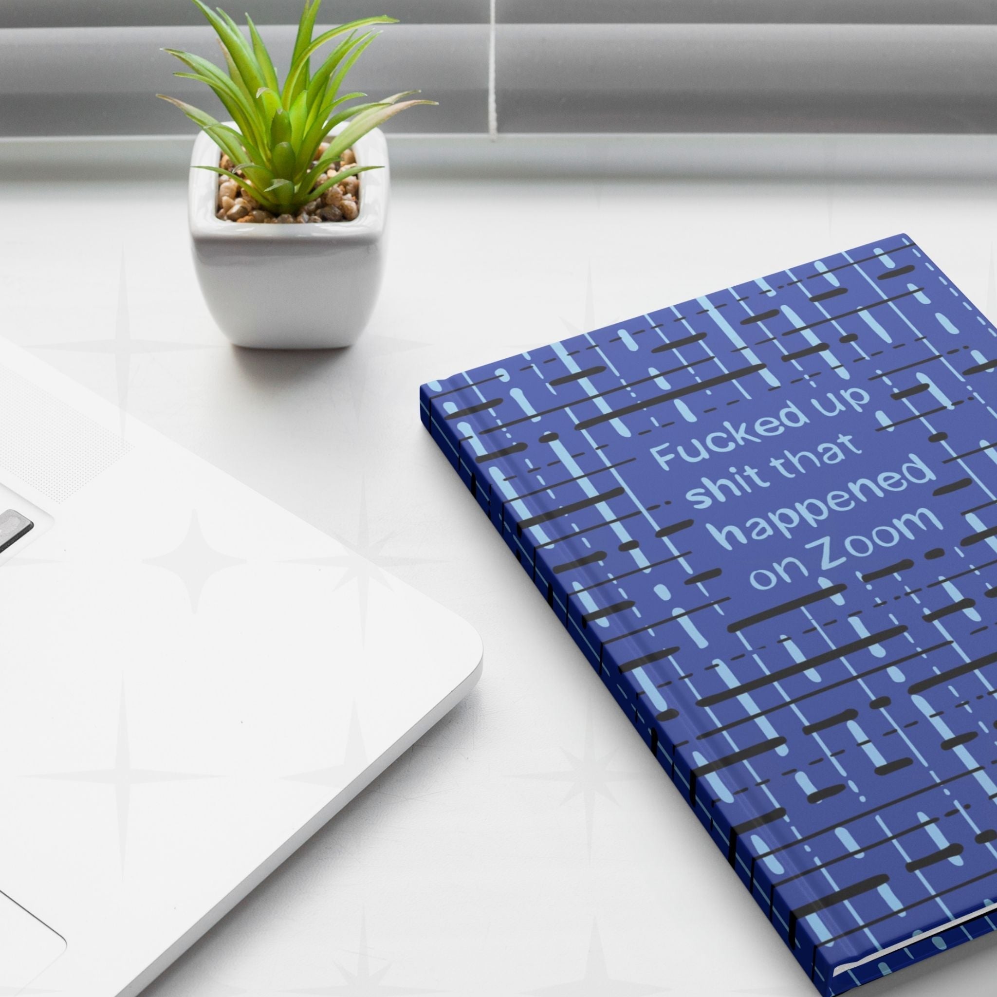 Zoom meeting profanity journal on white desk next to laptop and small succulent plant, work from home lifestyle setting