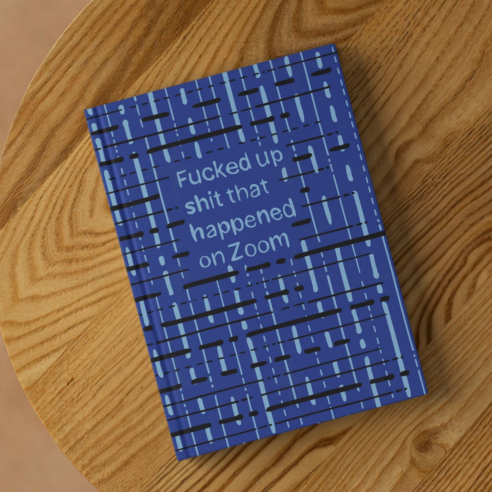 Funny Zoom profanity hardcover journal lying on round wooden surface showing front cover with cobalt blue abstract grid pattern