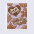 A greeting card with a gingerbread theme, featuring cookies, a gingerbread man, and the text &