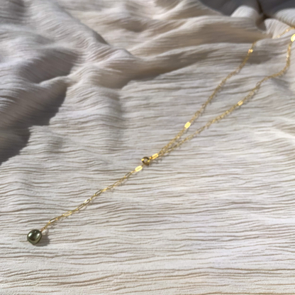 A gold-filled paperclip chain lariat necklace with a green fresh water pearl at the end, displayed on a textured white background.