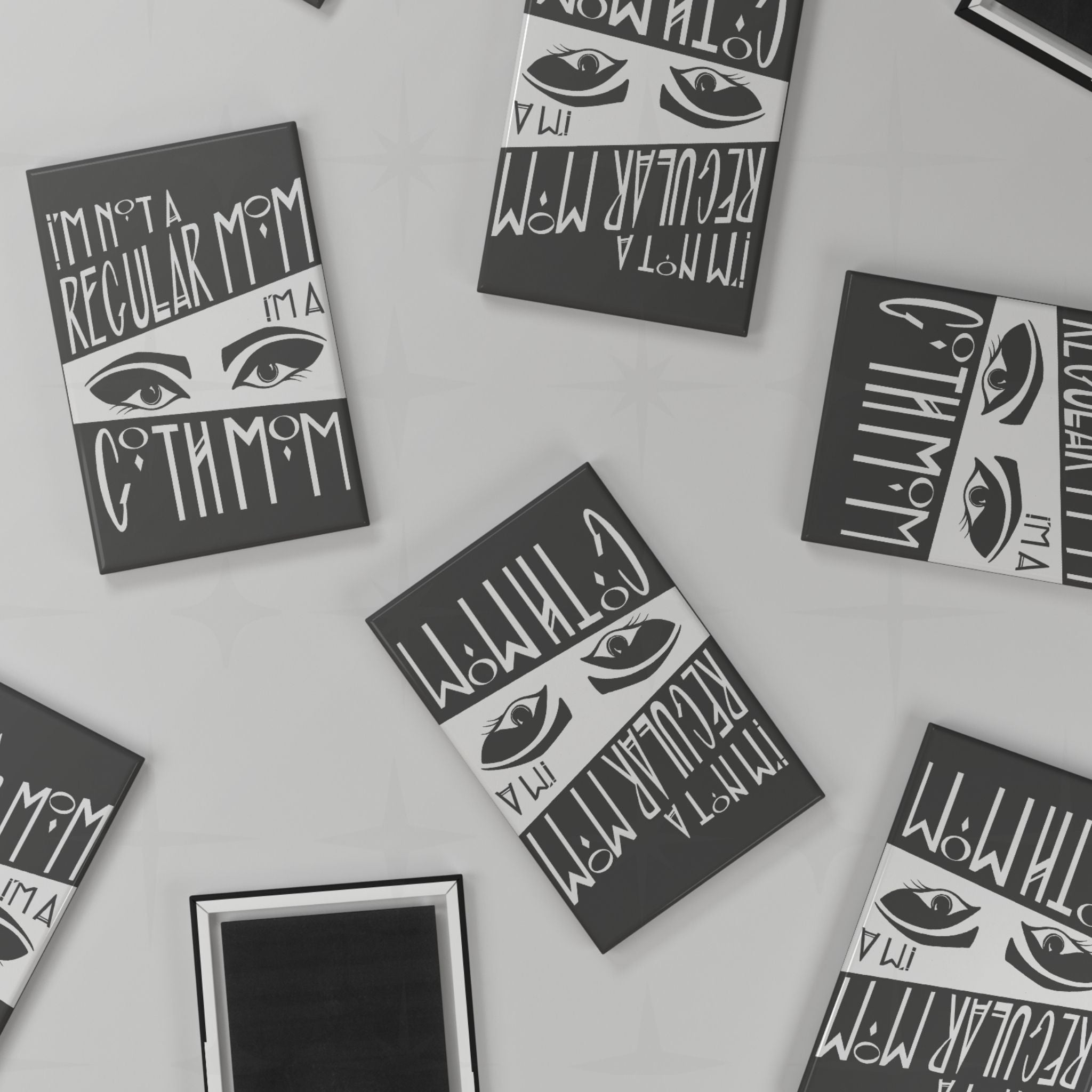 Flat lay of multiple goth mom magnets scattered at various angles on a light grey surface, showing both front design and black magnetic back