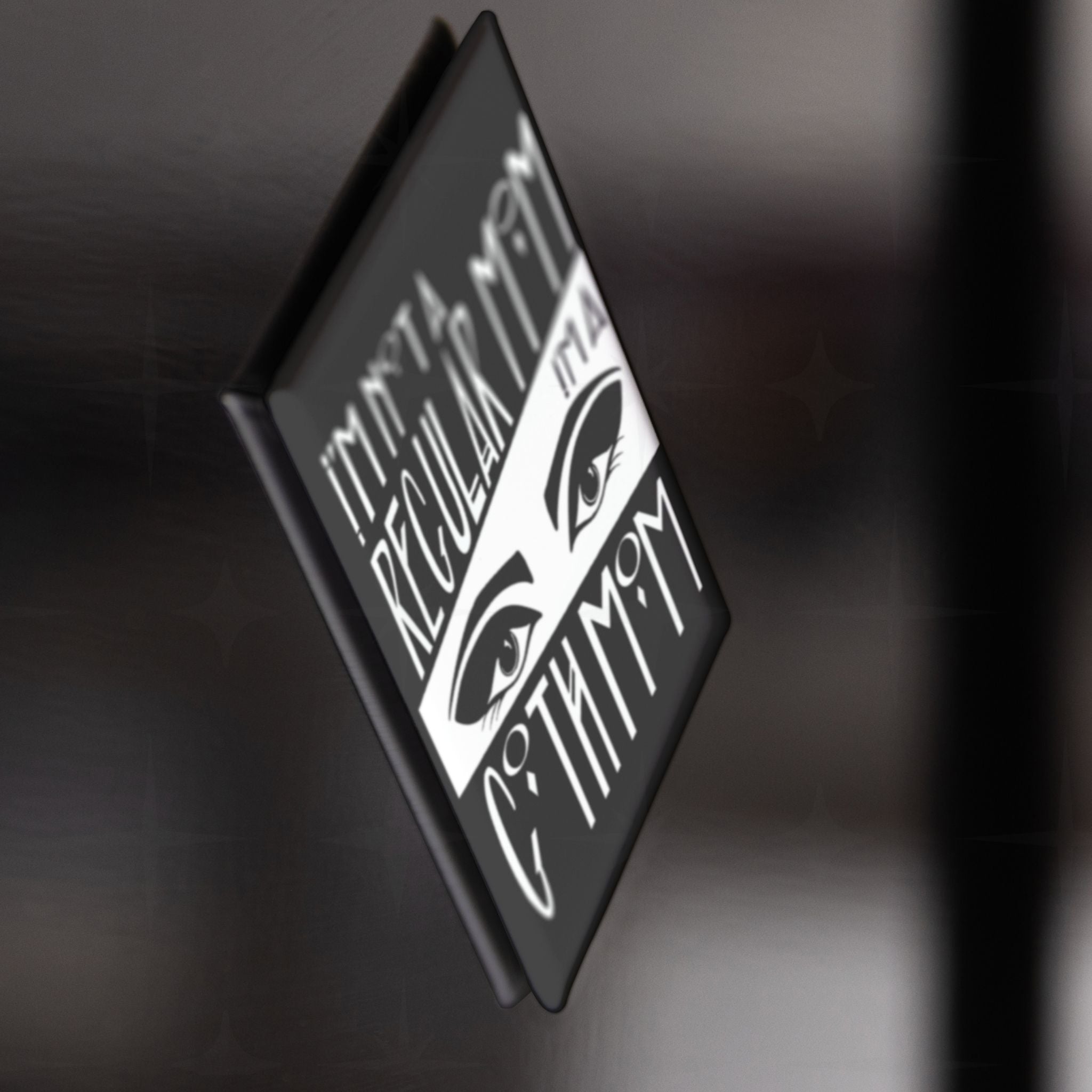 Side profile of the goth mom fridge magnet showing depth and glossy surface, attached to dark metallic surface