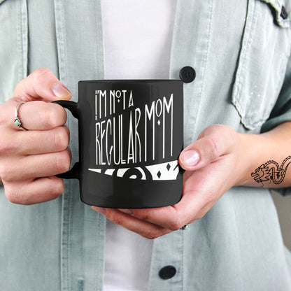 Tattooed hands holding black ceramic goth mom coffee mug with gothic hand lettering reading I&