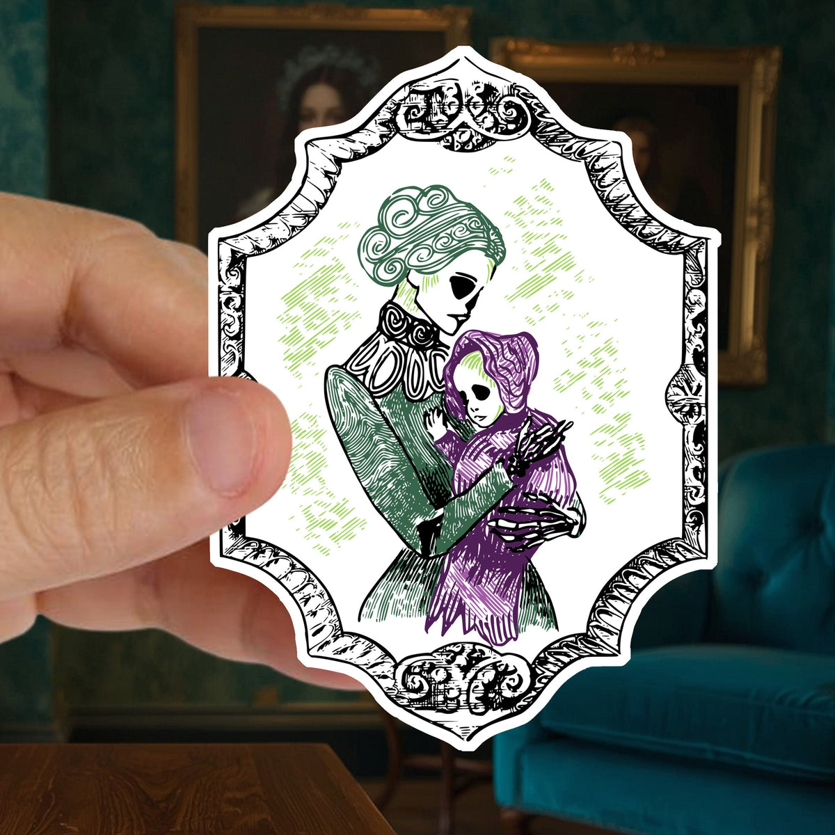 Hand holding a die cut skeleton sticker of a Victorian mother and baby against a green wall of gilt framed portraits