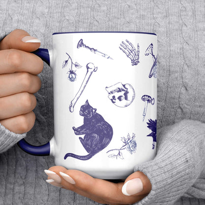 Blue and white delft pattern mug held in two hands showing a black cat, skull, and loose bones
