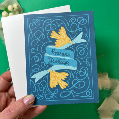 Hand holding a blue greeting card with yellow flowers and &
