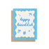Happy Hanukkah greeting card with blue text, yellow wavy border, and festive illustrations of a dreidel, stars, and bows. Card shown with kraft envelope.