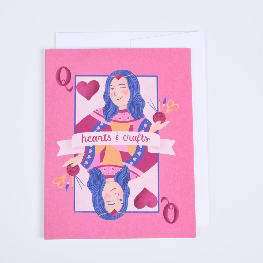A folded greeting card with a pink background featuring an illustration of a woman with blue hair and hearts, and text that reads &