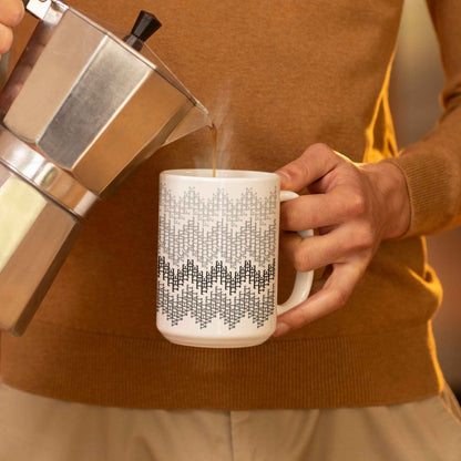 Coffee being poured from a moka pot into a gray hidden profanity mug, warm indoor morning setting