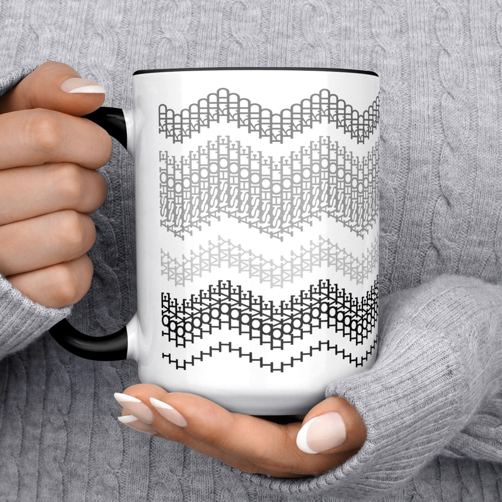 Lifestyle close-up of two hands in a gray cable-knit sweater holding the Gray and Black 15oz hidden message mug, with the hidden stitch text partially visible in the second band