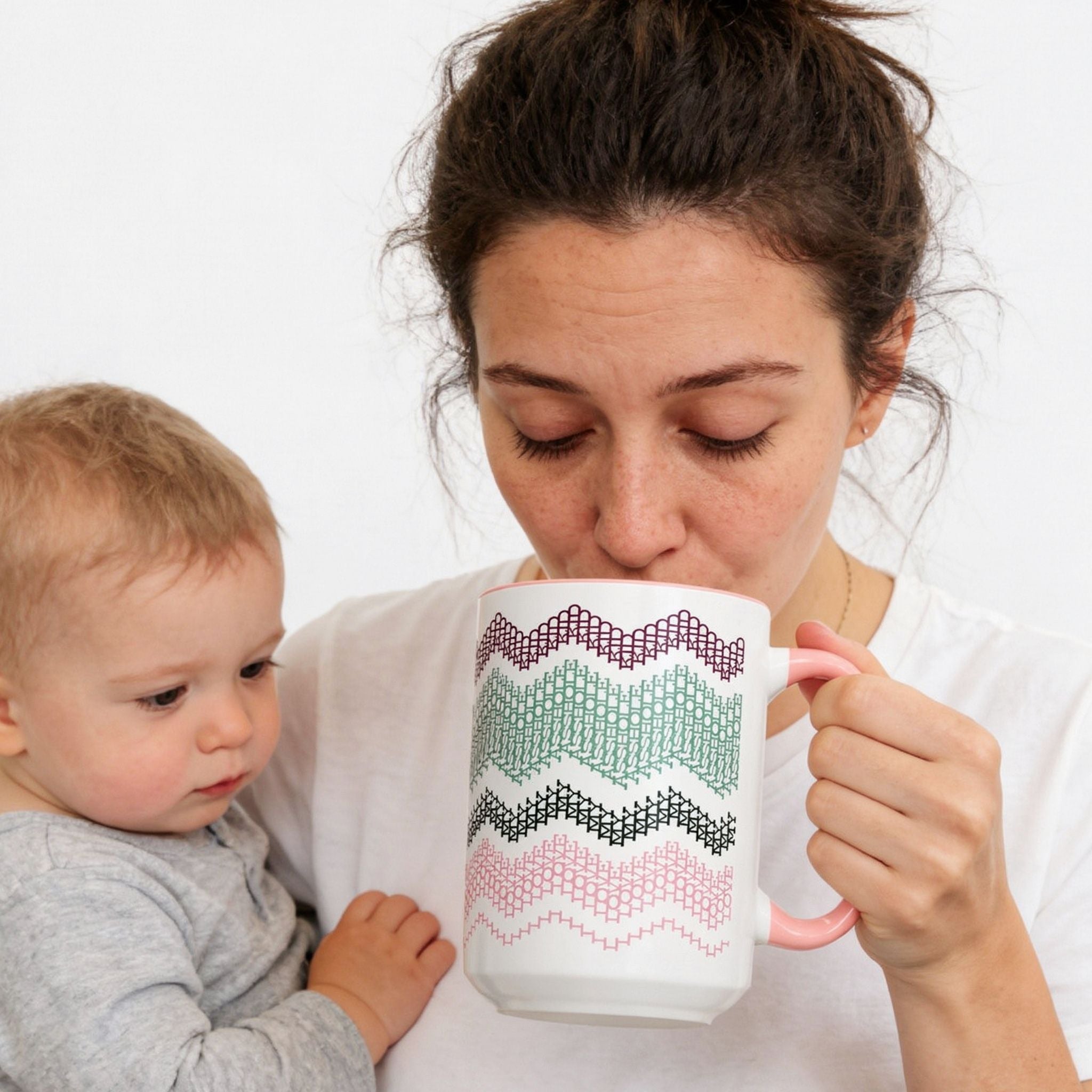 Lifestyle photo of a mother in a white t-shirt sipping from the Preppy Pink 15oz hidden message mug while holding a baby on her hip