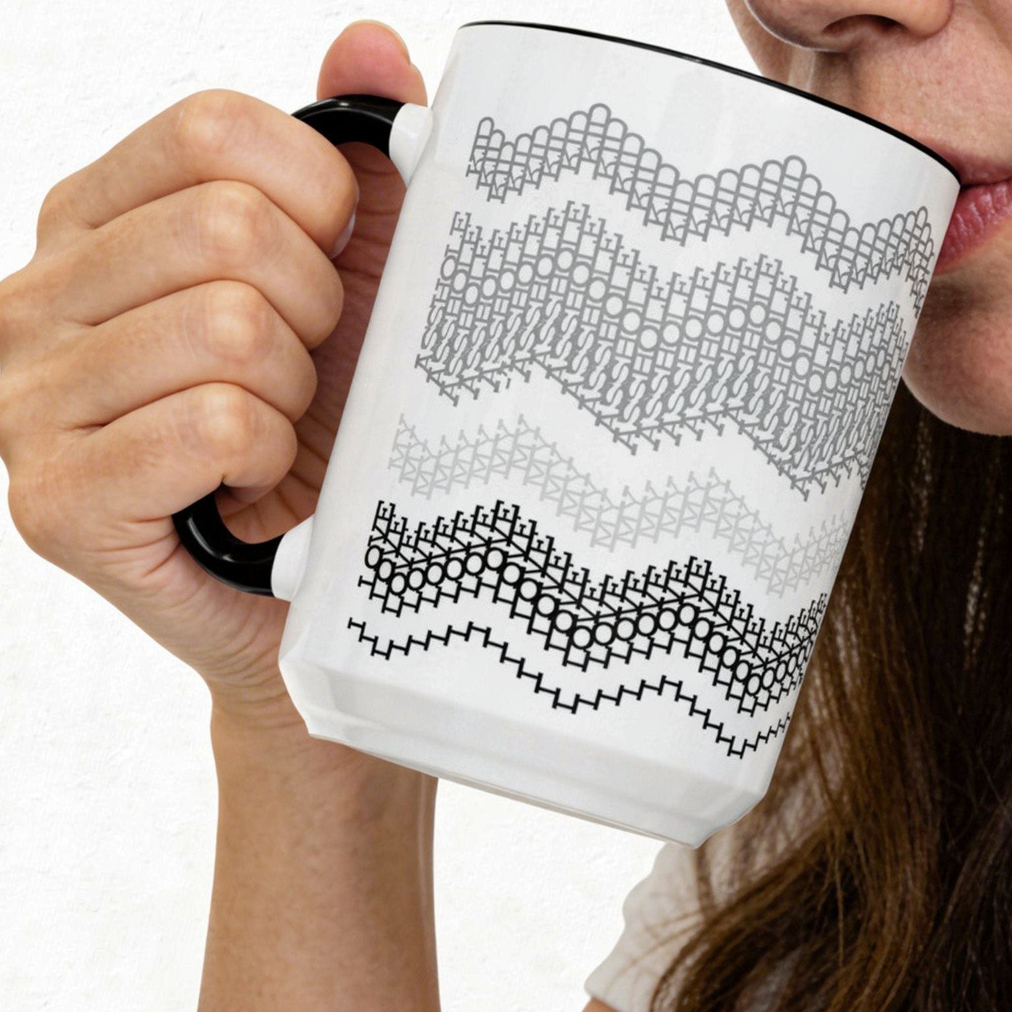 Lifestyle photo of a woman drinking from the Gray and Black 15oz hidden message mug, with one hand gripping the black handle and the fair isle chevron pattern facing forward