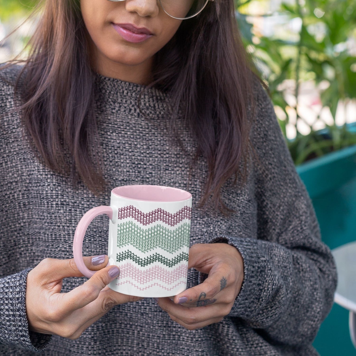 Preppy &amp; Pink hidden message mug 11oz held in both hands outdoors with green plants in background — showing the full burgundy, sage, forest green, and pink typographic pattern