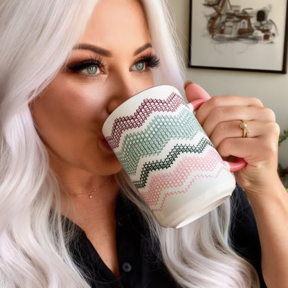 White-haired woman drinking from Preppy &amp; Pink hidden message mug — close portrait showing the burgundy, green, and pink fair isle typography pattern on the ceramic