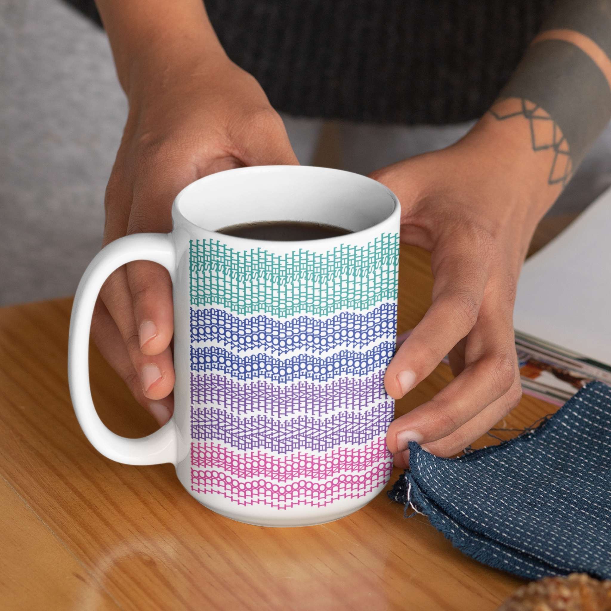 Hands holding bright stripes hidden message embroidery mug filled with coffee on a wooden table

