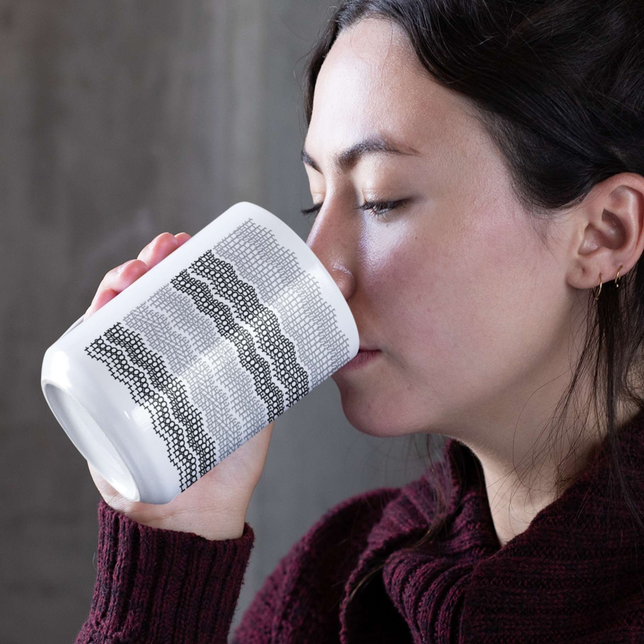 Woman drinking from gray stripes hidden message embroidery mug, wearing burgundy sweater