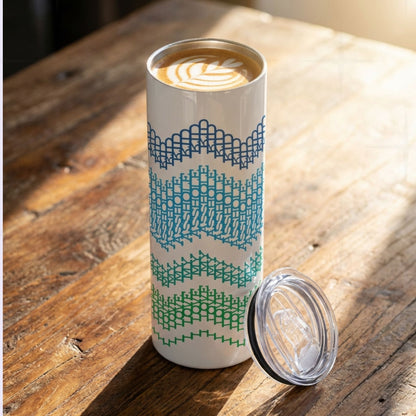 Ocean Stripes hidden message tumbler on a rustic wood table with latte art visible inside — navy, teal, and green cross-stitch stripe pattern, lid resting beside it