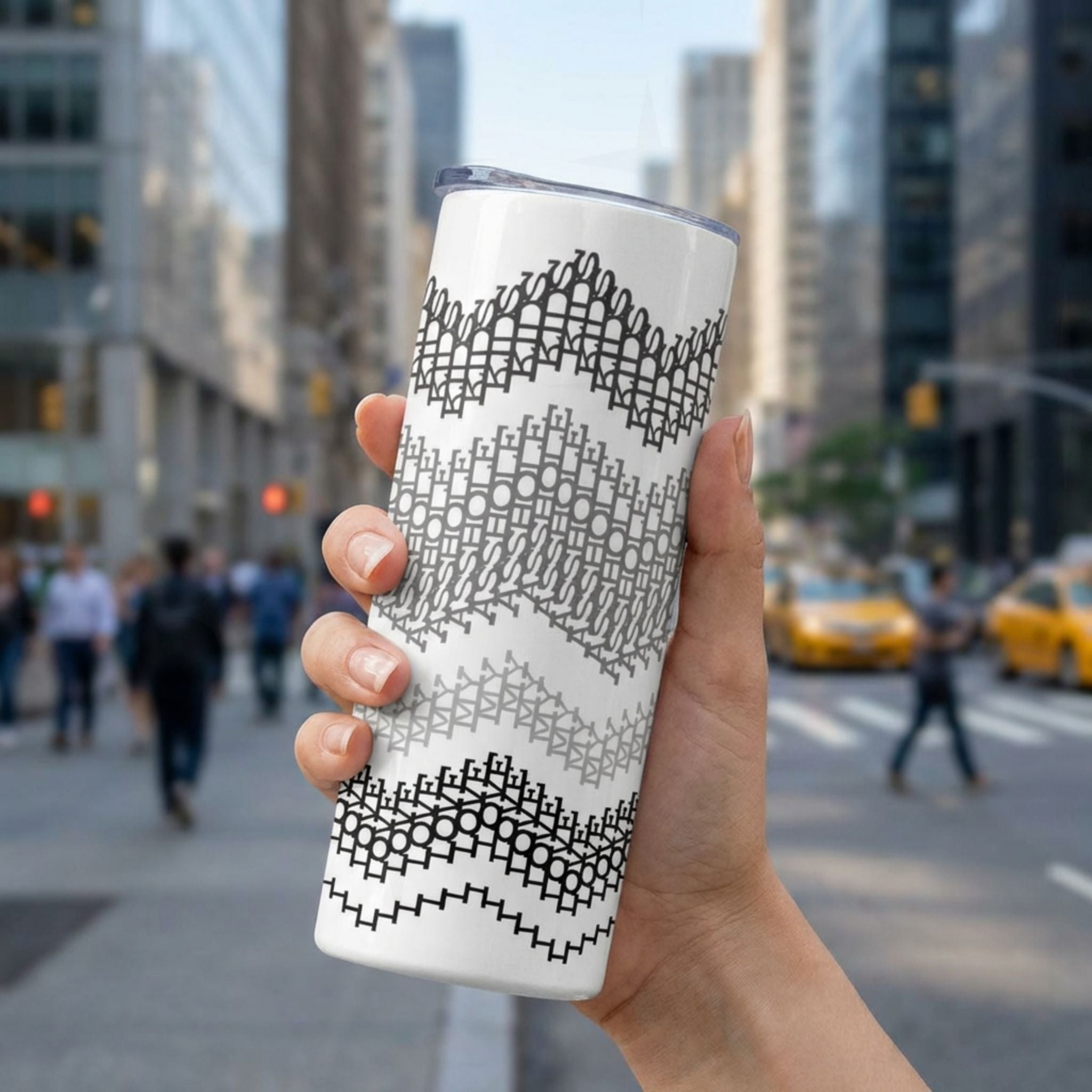 20 oz hidden message skinny tumbler held in an urban setting, gray stripes colorway — four horizontal chevron wave bands in black, charcoal, gray, and light gray on white