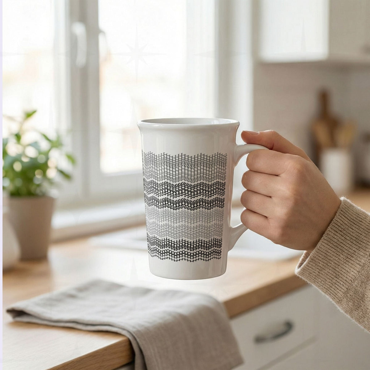 Hand holding gray stripes hidden profanity latte mug in bright kitchen, knit stitch text pattern in light gray to charcoal on white ceramic
