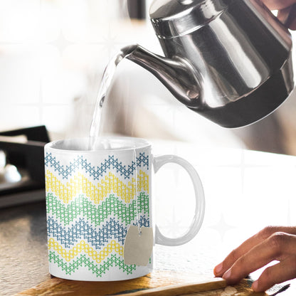 Hidden message cross stitch mug with Go Fuck Yourself text visible in chevron pattern, tea bag inside, hot water being poured from kettle