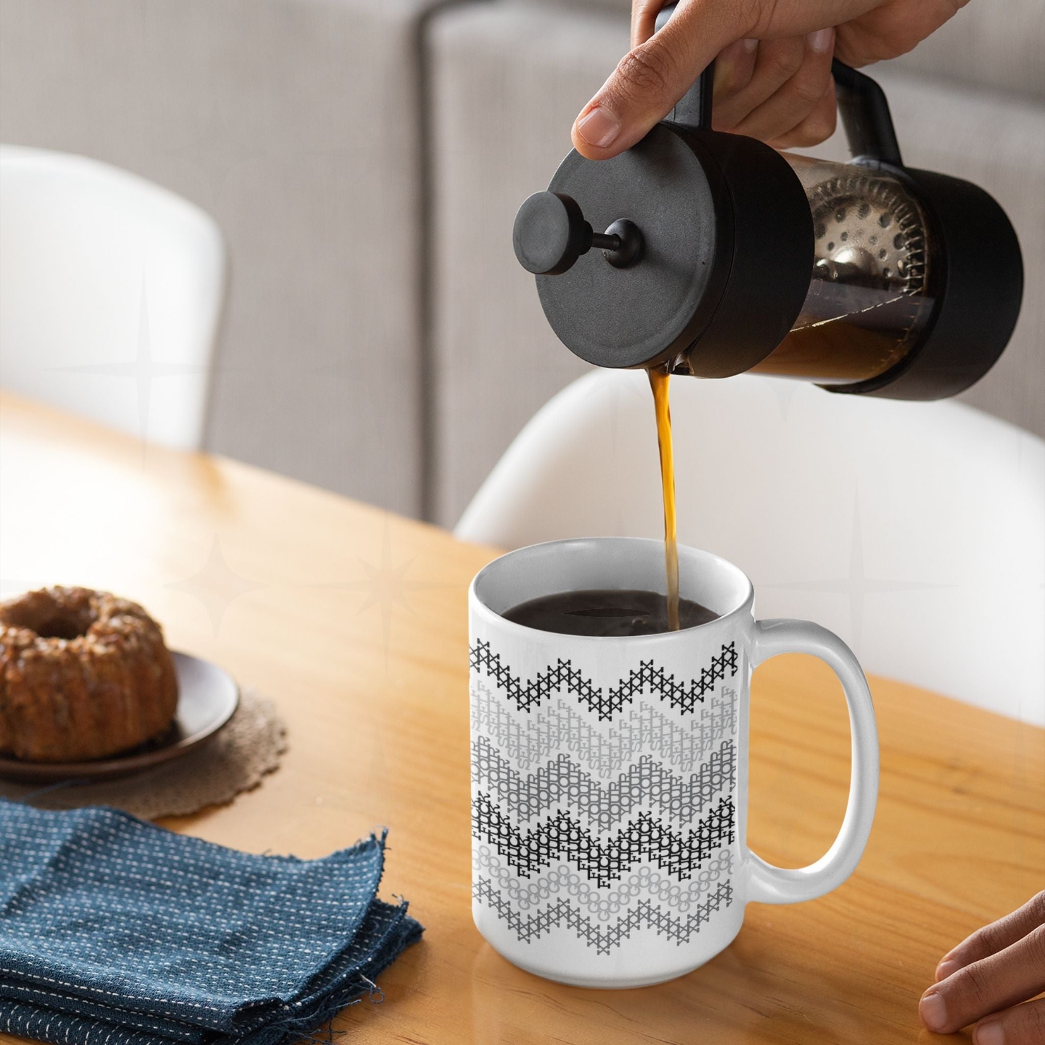 Hidden profanity coffee mug gray stripe cross stitch pattern being filled with French press coffee on a wooden breakfast table