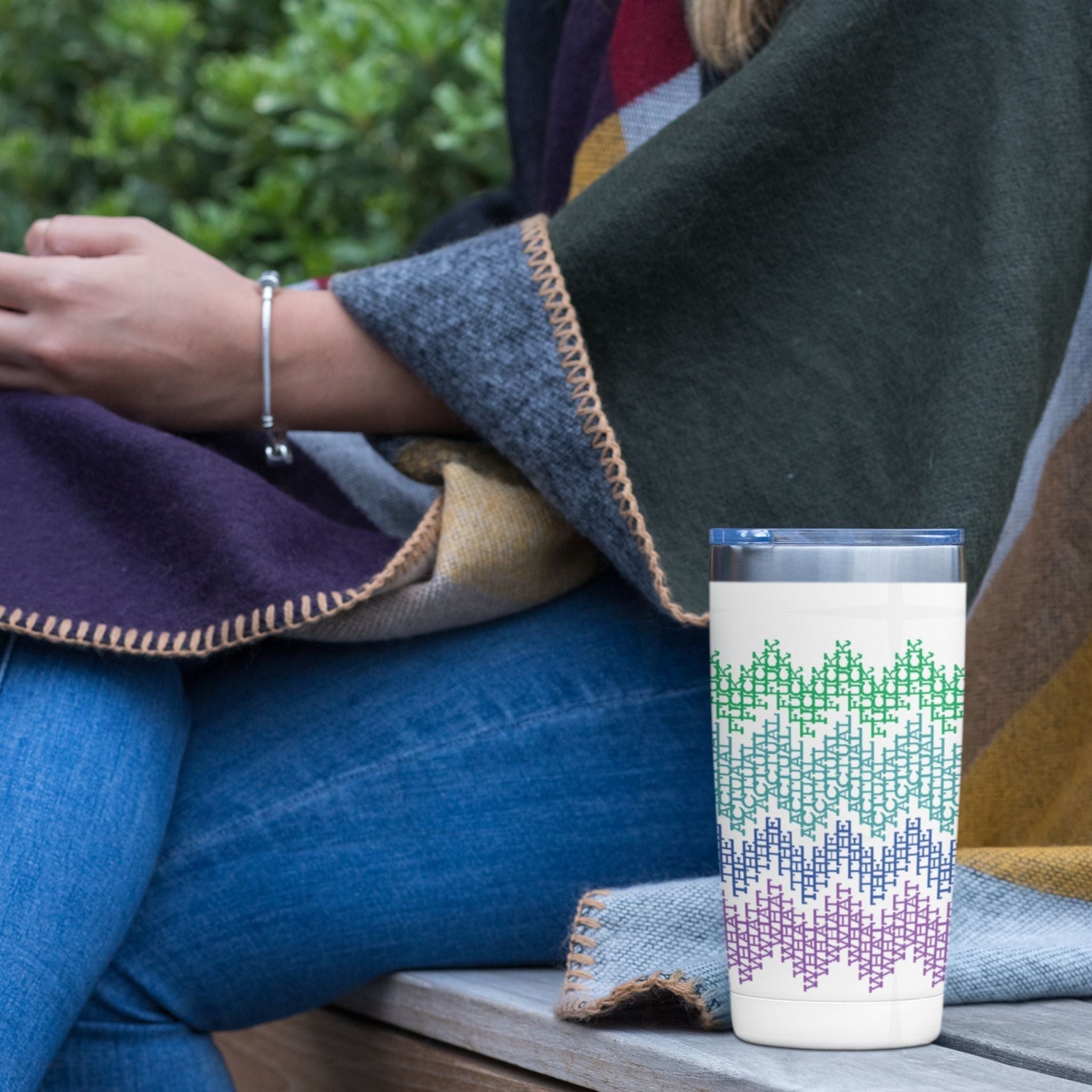 Bright stripes hidden message tumbler on a park bench beside person in jeans and blanket, outdoor lifestyle photo showing green teal blue purple pattern