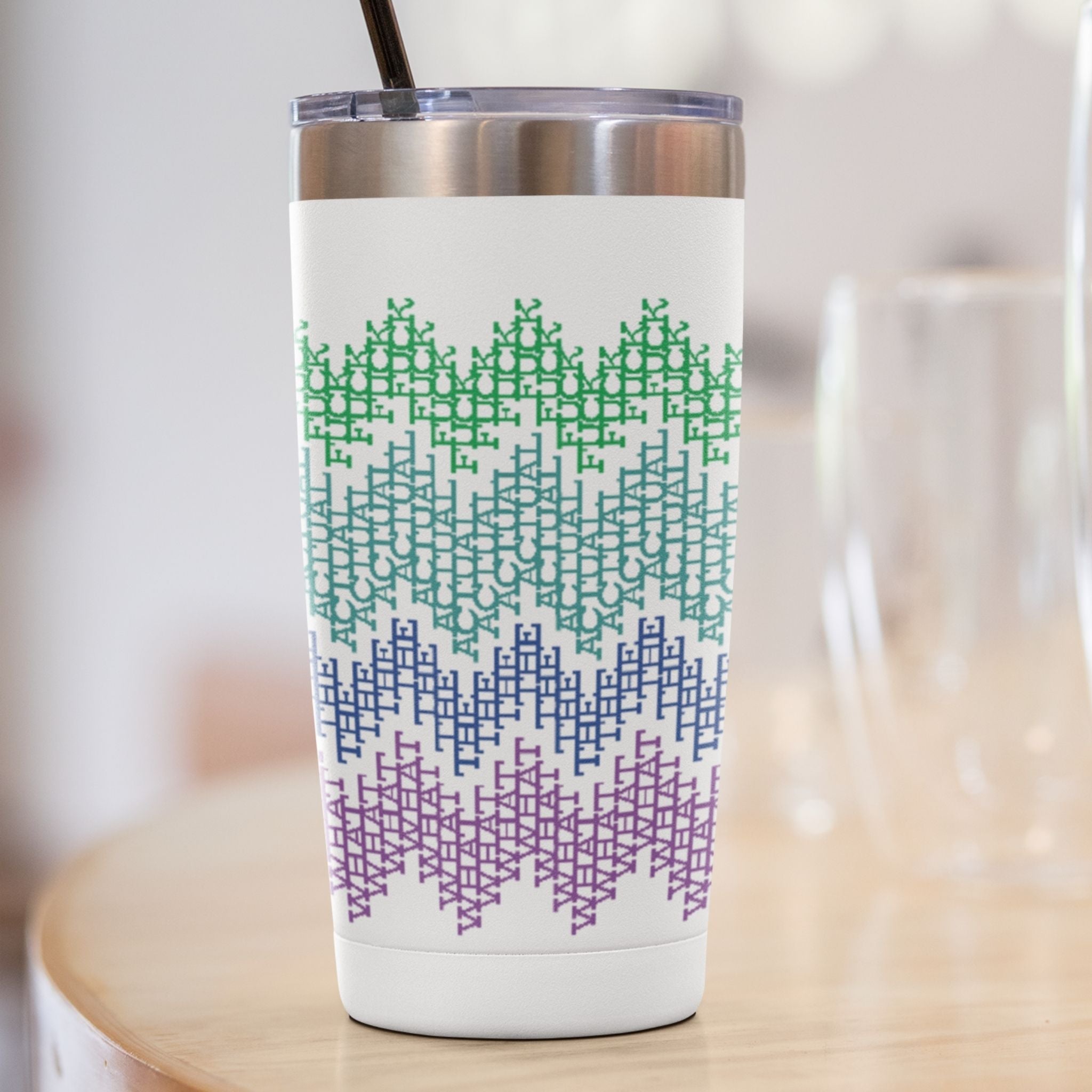 Bright stripes hidden profanity tumbler with straw on light wooden table, close-up showing green teal blue purple cross-stitch text pattern