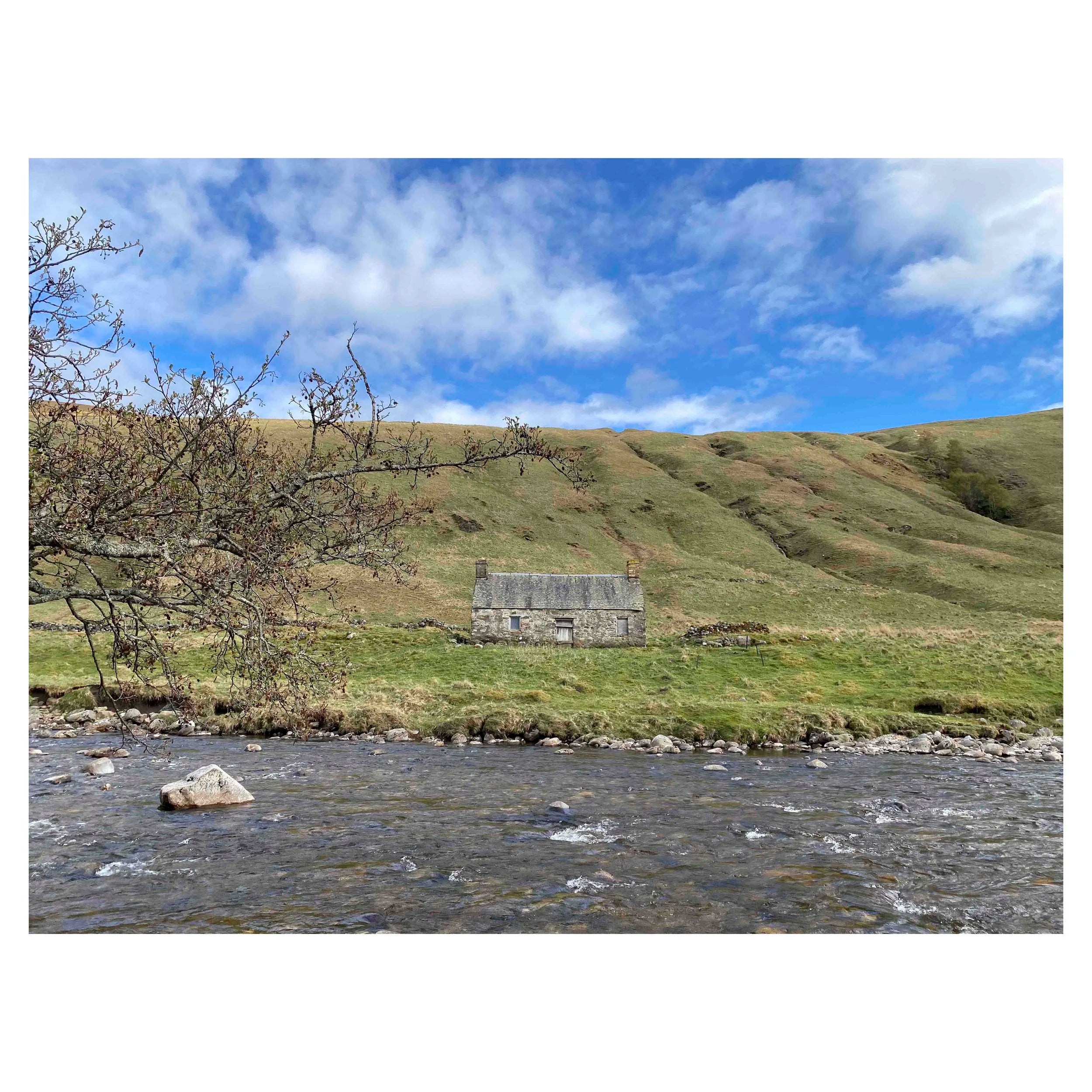 Photograph of a stone cottage under a bright blue sky on the bank of the River Tilt in Scotland.