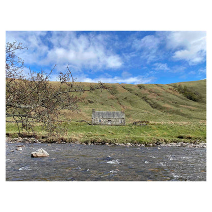 Photograph of a stone cottage under a bright blue sky on the bank of the River Tilt in Scotland.
