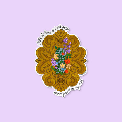 Vinyl sticker with ornate golden frame, blooming flowers, and the text “I hate it here so I will go to secret gardens in my mind.”