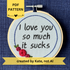 PDF pattern created by Kate, not AI. "I love you so much it sucks." Quote hand embroidered in handwriting font in black embroidery thread. Around the text is a floral wreath of a blue ring, red roses and green leaves. Fabric is light blue, and completed embroidery is displayed in a light wood embroidery hoop.
