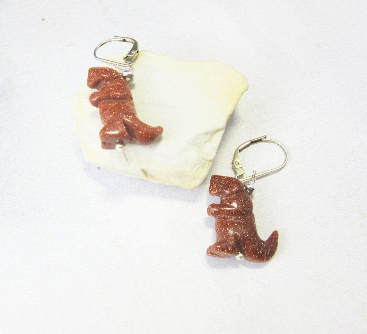 Tyrannosaurus rex earrings featuring intricate carvings and a rust goldstone finish, perfect for a paleontologist gift.