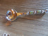 The Artisan Crafted Herb & Bath Salt Spoon Color Changing Mood Bead Scoop, with its vibrant patterns, silver accents, and decorative handle, rests on a wooden surface. Its round bowl shines beautifully, reflecting the surroundings.